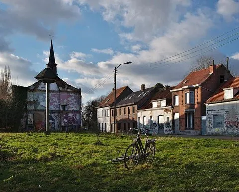 Una bicicleta parada sobre el pasto; al fondo, una fila de casas y una iglesia pequeña.