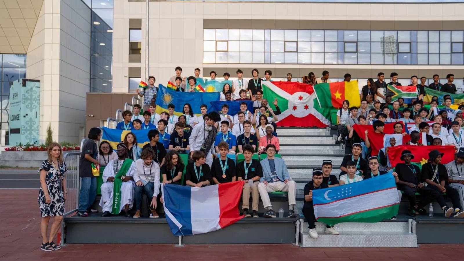 Foto grupal de estudiantes de muchos países en unas graderías, con sus banderas; arriba a la izquierda, la delegación de Bolivia con banderas bolivianas