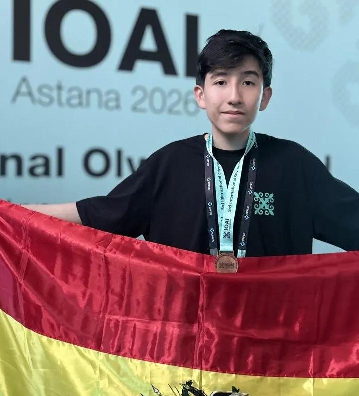 Nicolás Bravo con la medalla de bronce y la bandera de Bolivia frente al cartel de la IOAI Astana 2026